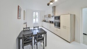 A modern kitchen with white cabinets, a dining table with chairs, and a large window providing natural light. - Appartment the House of Hera (Vierzon)