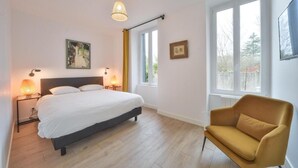 A bedroom with a bed, bedside lamps, a window, a sofa, and artwork on the walls. - Appartment the House of Hera (Vierzon)