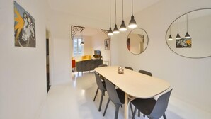 Een moderne eetruimte met een lange tafel, stoelen, hanglampen en kunst aan de muren.