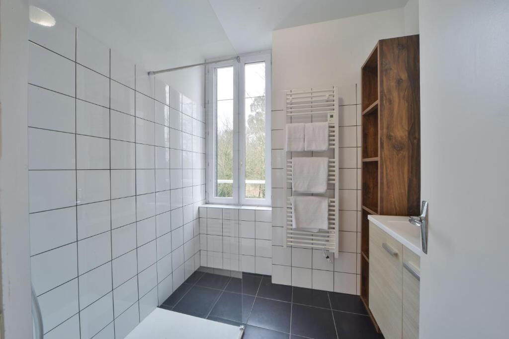 Une salle de bain moderne avec des carreaux blancs, un sol noir, une fenêtre, un porte-serviettes et un meuble en bois.