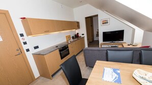 A modern kitchen with wooden cabinets, a built-in oven, and a dining area with a table and chairs. - Hrimland - Luxury Apartment for 2 people (Akureyri)