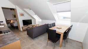 A modern loft apartment with a dining area, a sofa, a TV, and a kitchen with a built-in stove. - Hrimland - Luxury Apartment for 2 people (Akureyri)