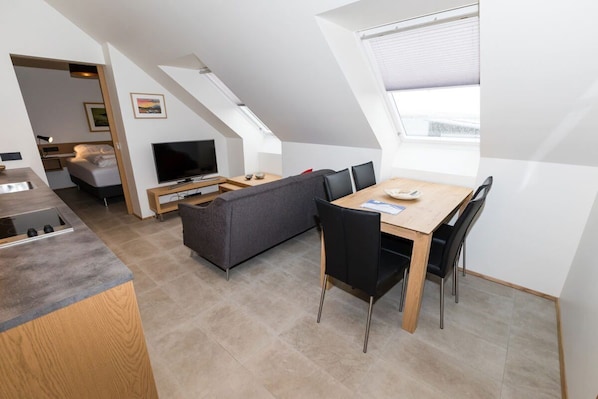 A modern loft apartment with a dining area, a sofa, a TV, and a kitchen with a built-in stove.