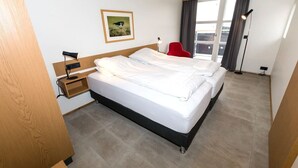 A hotel room with a double bed, a red chair, a desk with a lamp, a picture on the wall, and a large window with curtains. - Hrimland - Luxury Apartment for 2 people (Akureyri)