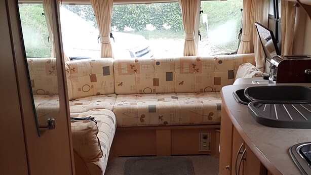A compact RV interior with a kitchenette, a dining area, and a sleeping berth. - Lovely Caravan Near Notts and Newark (Newark)