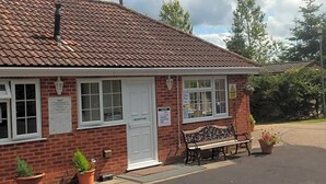 A small brick building with a tiled roof, a reception desk, and a bench outside. - Lovely Caravan Near Notts and Newark (Newark)