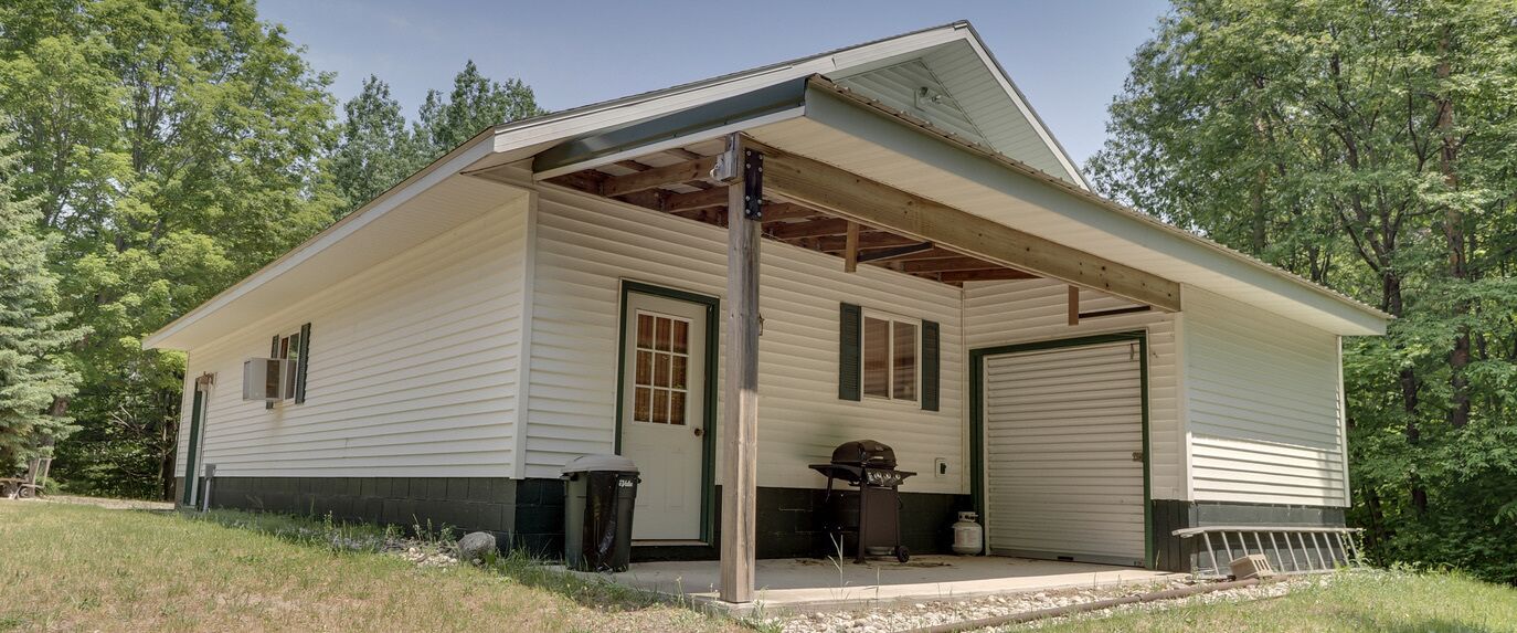 Een gelijkvloers huis met een overdekte veranda, een garage en een klein barbecuegedeelte.