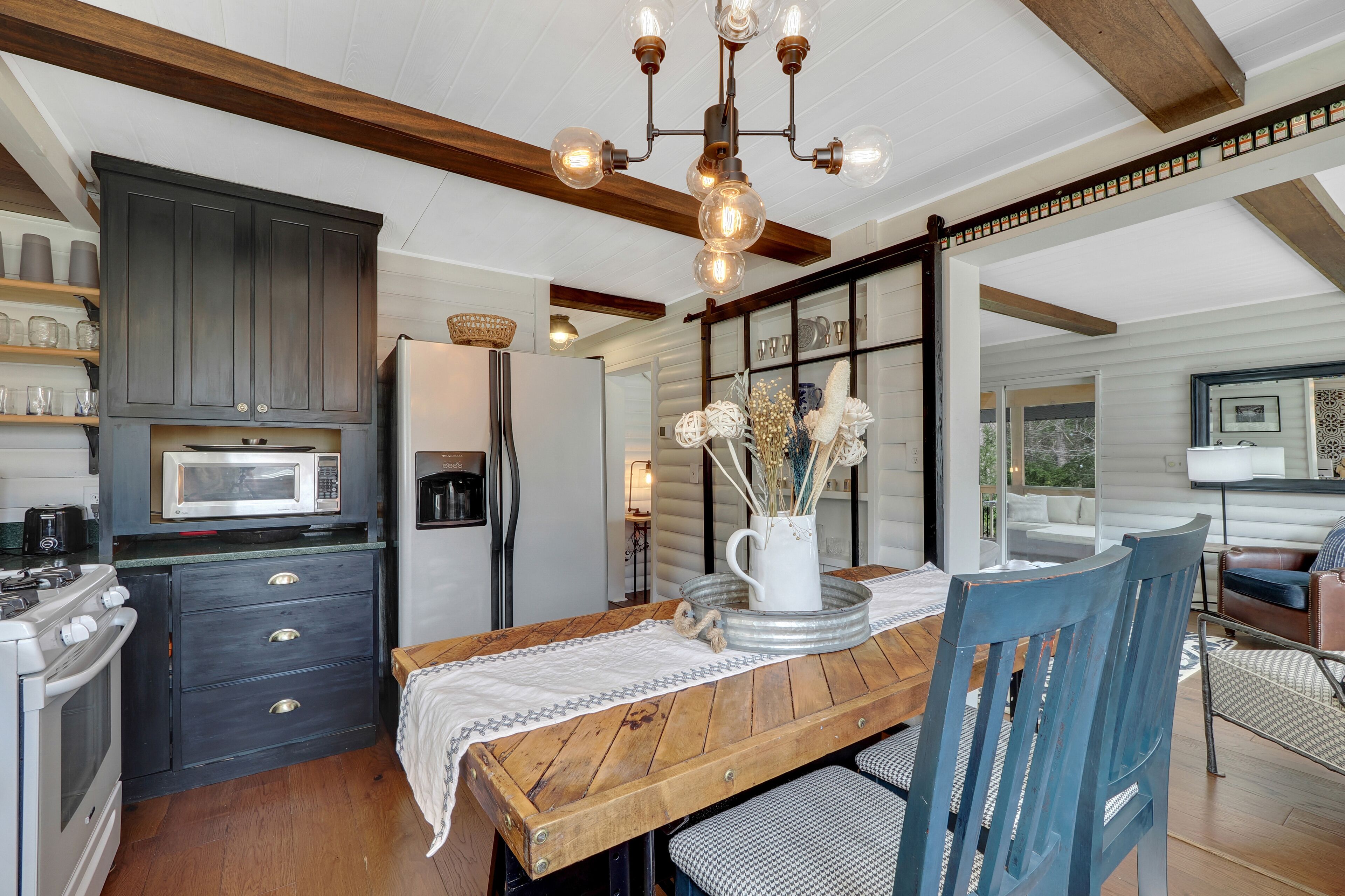 A kitchen with dark cabinets, a wooden dining table, and a chandelier.