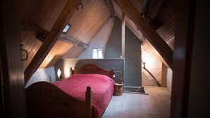 Un dormitorio con cama de madera, mesita de noche, lámpara de pared y ventana con vistas al exterior.