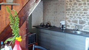 Una cocina con pared de piedra, vigas de madera, estufa a gas y cafetera.