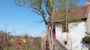 Un edificio rústico con fachada blanca y marcos de ventana rojos, rodeado de árboles y un cielo azul despejado.