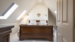 Ein Schlafzimmer mit einem hölzernen Bett, einem weißen, flauschigen Teppich, einer Wanddekoration in Herzform und Dachfenstern.
