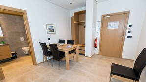 A hotel room with a wooden dining table, four chairs, a small kitchenette, a toilet, a closet, and a door with a fire extinguisher. - Hrimland - Luxury Apartment for 2 persons (Akureyri)
