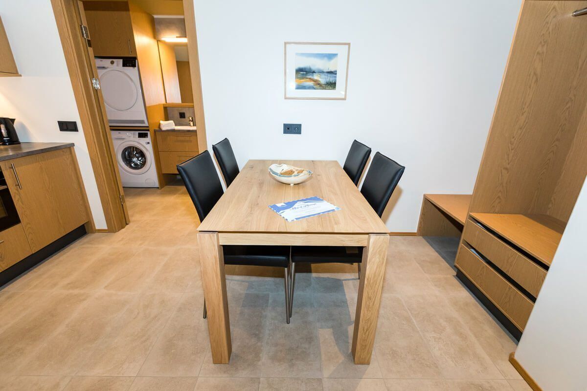 A compact kitchen with a washing machine, a dining table with chairs, and a small bench.