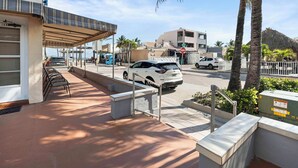A street view with a covered outdoor seating area, a white car parked on the street, and a building with a sign. - Expo Motel (Hollywood)