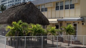 A building with a thatched-roof structure in front, surrounded by palm trees and a white fence. - Expo Motel (Hollywood)