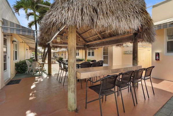 An outdoor dining area with a thatched roof, wooden tables, and chairs. - Expo Motel (Hollywood)