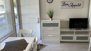 A modern living room with a dining area, white furniture, a clock, a plant, and a TV on a stand. - Expo Motel (Hollywood)