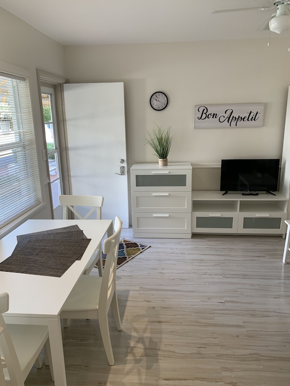 A modern living room with a dining area, white furniture, a clock, a plant, and a TV on a stand. - Expo Motel (Hollywood)