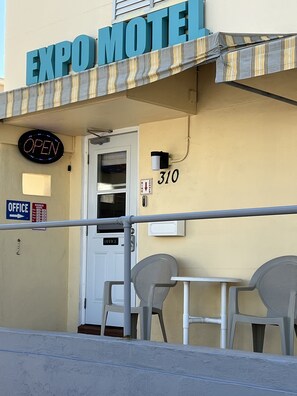 The exterior of the Expo Motel, featuring a neon 'OPEN' sign, a number '310' on the wall, and a sign indicating an 'OFFICE' to the left.