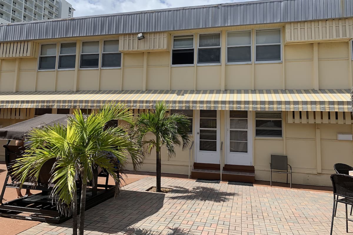 A building with a flat roof, a striped awning, and a paved patio area with palm trees and outdoor seating.