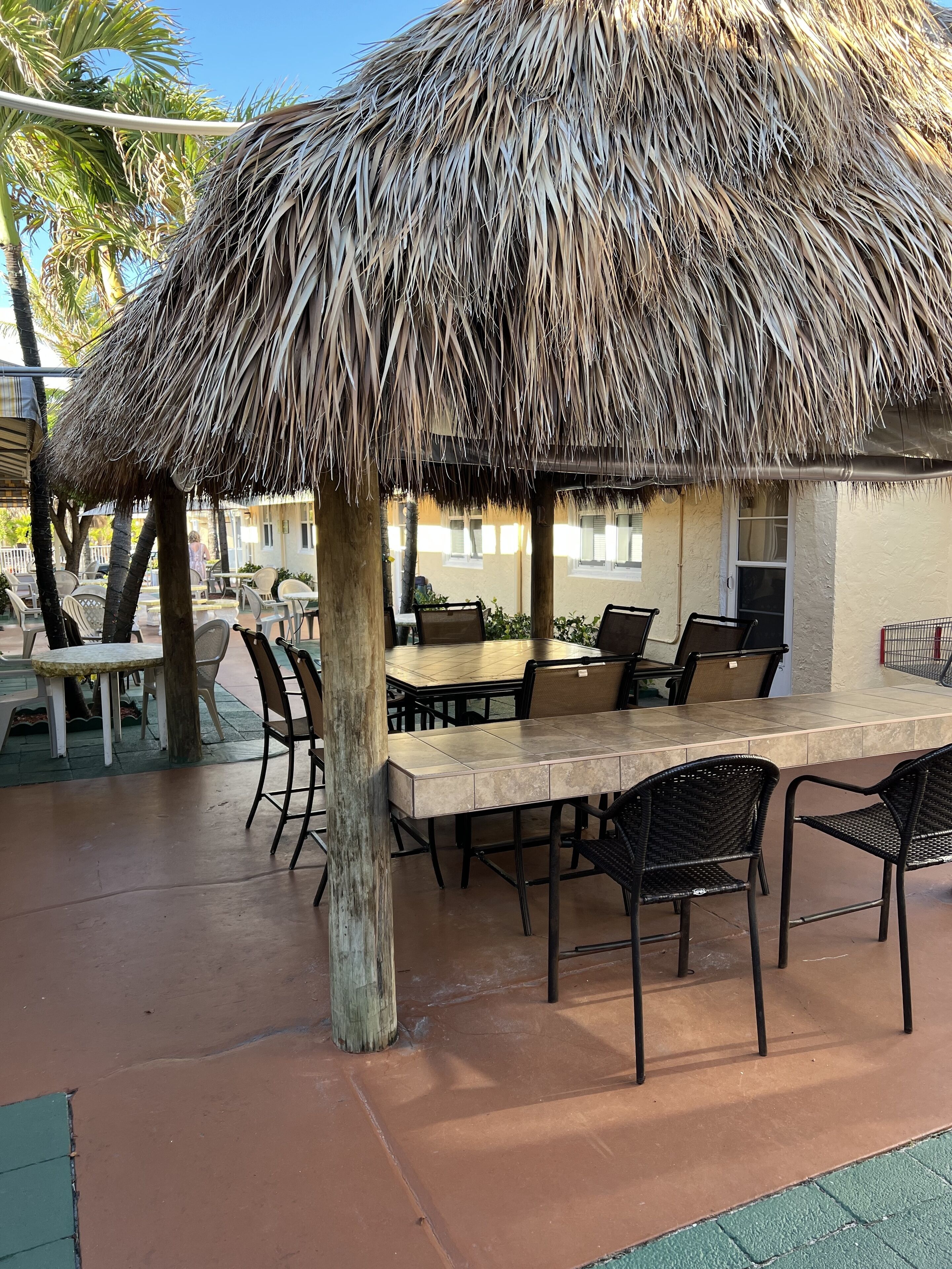 An outdoor dining area with a thatched roof, tables, and chairs.
