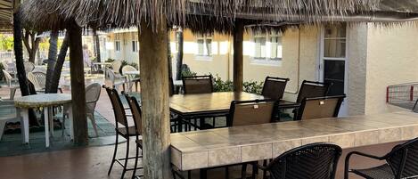 An outdoor dining area with a thatched roof, tables, and chairs.