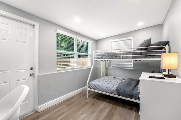 A room with a bunk bed, a desk with a lamp, a chair, and a window with blinds. - Remodeled 3BR, 6 Min to Busch Gardens | Fenced Yard, Monthly Stays Welcome (Tampa)