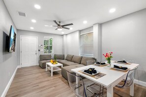 A modern living room with a sofa, a coffee table, and a dining table set for two. - Remodeled 3BR, 6 Min to Busch Gardens | Fenced Yard, Monthly Stays Welcome (Tampa)