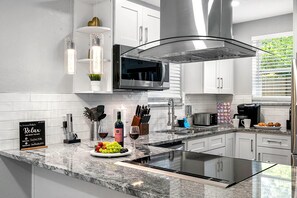 A modern kitchen with white cabinetry, a built-in microwave, a stainless steel range hood, and a granite countertop. - Remodeled 3BR, 6 Min to Busch Gardens | Fenced Yard, Monthly Stays Welcome (Tampa)