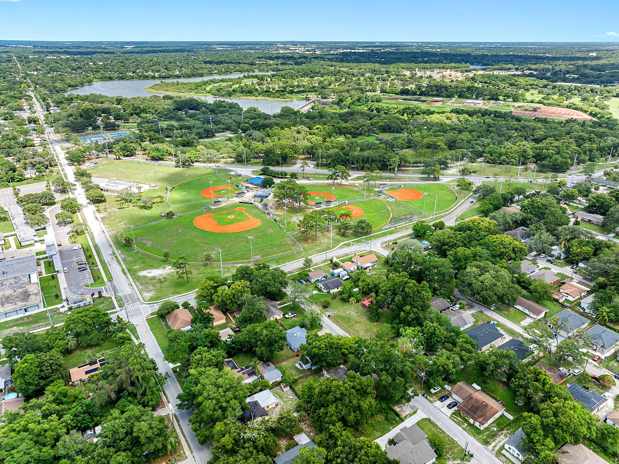 An aerial view of a baseball field surrounded by residential houses and a parking lot.