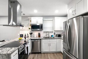 A modern kitchen with stainless steel appliances, white cabinetry, and a central island. - Remodeled 3BR, 6 Min to Busch Gardens | Fenced Yard, Monthly Stays Welcome (Tampa)