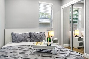 A bedroom with a bed, two bedside tables, a nightstand, a mirror, and a window with blinds. - Remodeled 3BR, 6 Min to Busch Gardens | Fenced Yard, Monthly Stays Welcome (Tampa)