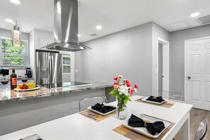A modern kitchen with a central island, stainless steel appliances, and a dining area set for a meal. - Remodeled 3BR, 6 Min to Busch Gardens | Fenced Yard, Monthly Stays Welcome (Tampa)