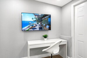A white desk with a chair, a potted plant, and a large framed picture of a beach scene. - Remodeled 3BR, 6 Min to Busch Gardens | Fenced Yard, Monthly Stays Welcome (Tampa)