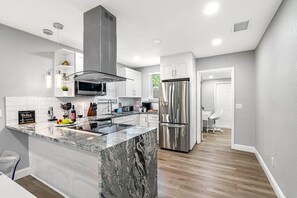 A modern kitchen with a central island, stainless steel appliances, and a white backsplash. - Remodeled 3BR, 6 Min to Busch Gardens | Fenced Yard, Monthly Stays Welcome (Tampa)