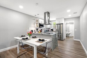 A modern kitchen with white cabinetry, stainless steel appliances, and a dining area with a white table and chairs. - Remodeled 3BR, 6 Min to Busch Gardens | Fenced Yard, Monthly Stays Welcome (Tampa)