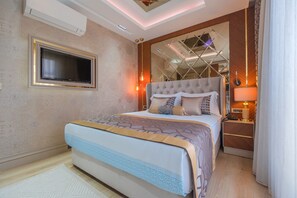 A modern hotel room with a large bed, a TV mounted on the wall, and a nightstand with a lamp. - Elysium Deluxe Suites  (Antalya)