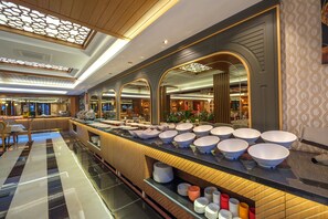 A buffet area with multiple bowls and plates, a long counter, and a patterned wall. - Elysium Deluxe Suites  (Antalya)