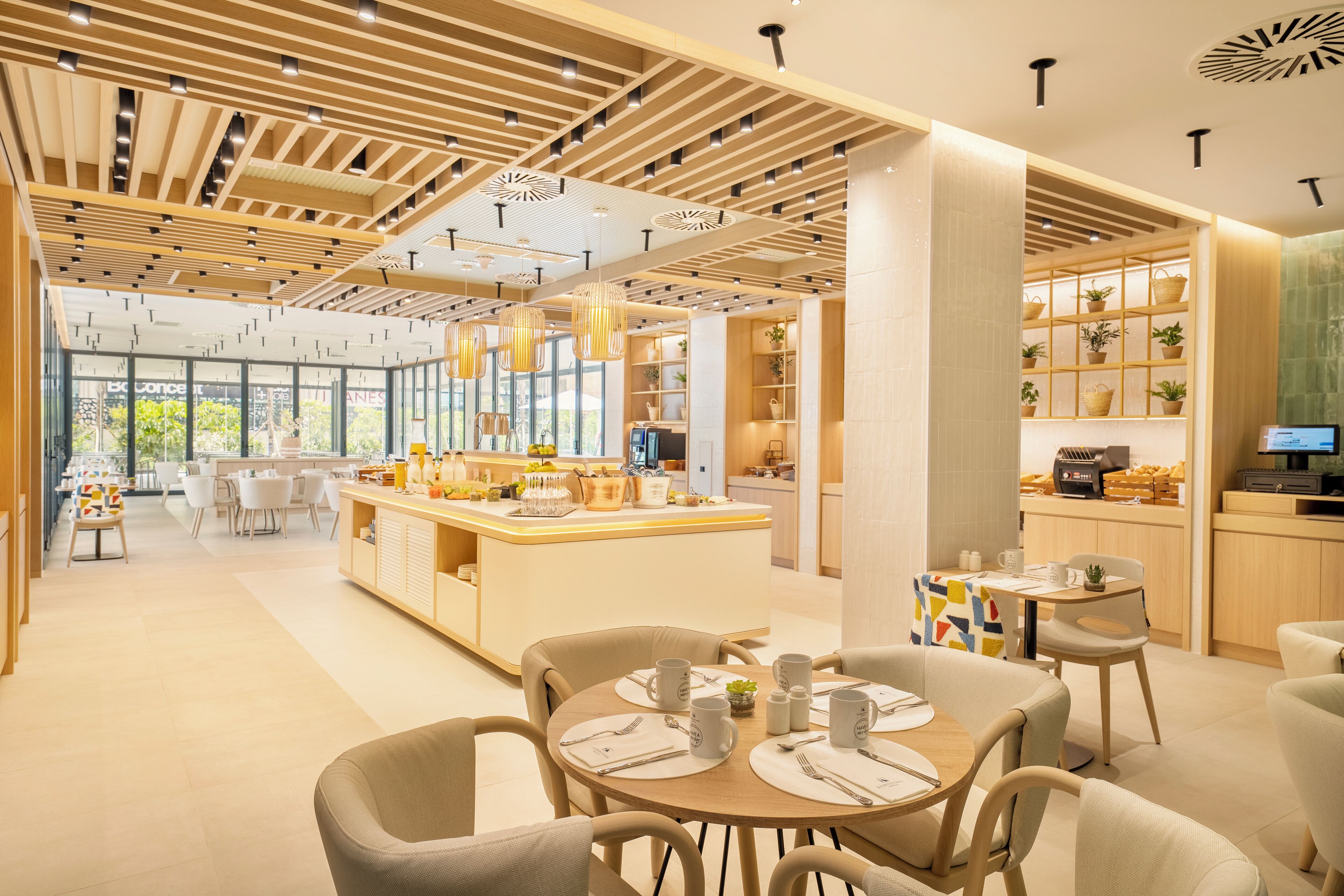 A modern hotel lobby with a central island, seating areas, and a kitchen visible in the background.