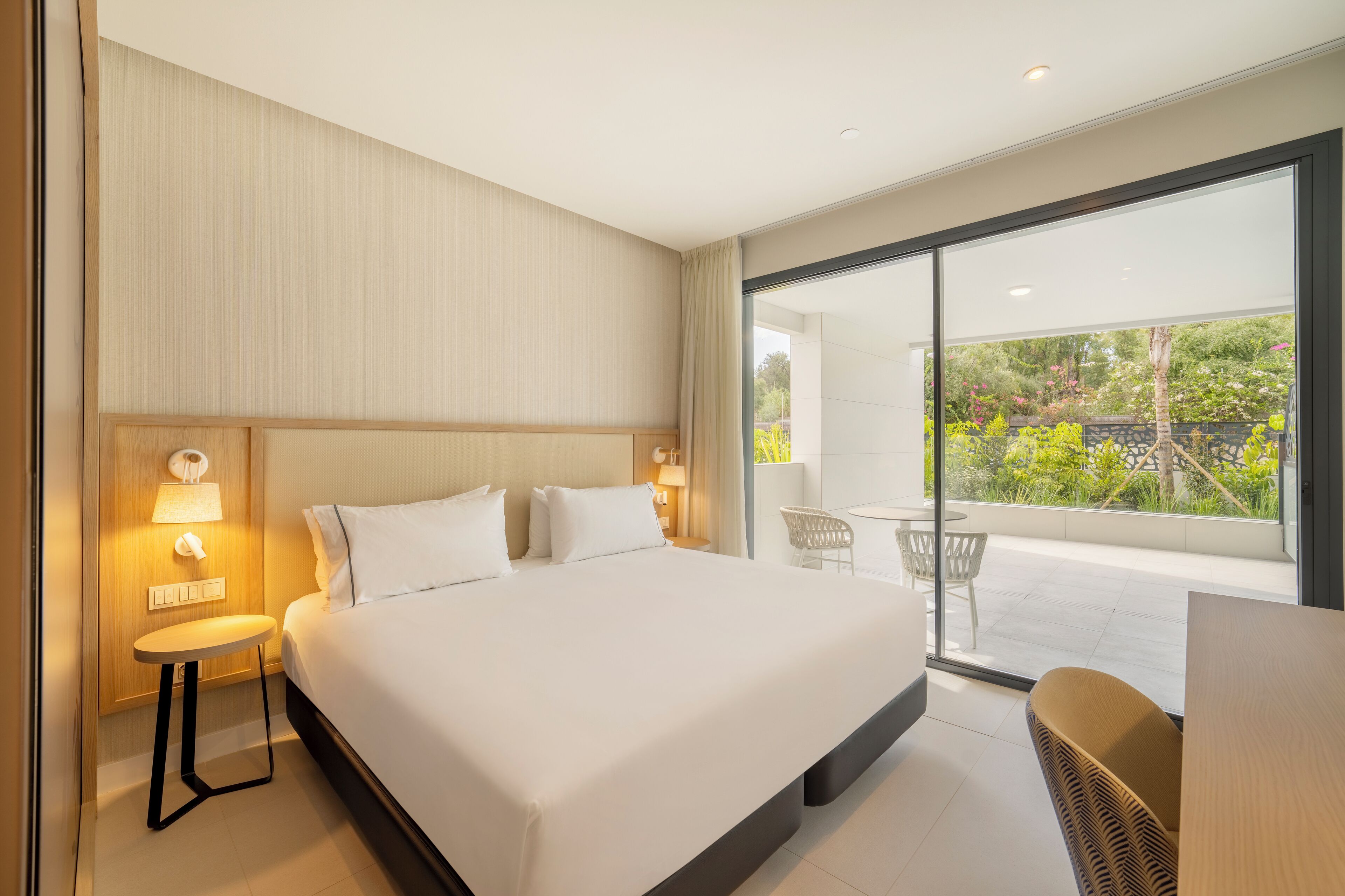 Une chambre d’hôtel moderne avec un grand lit, des lampes de chevet, une petite table et une vue sur le balcon extérieur.