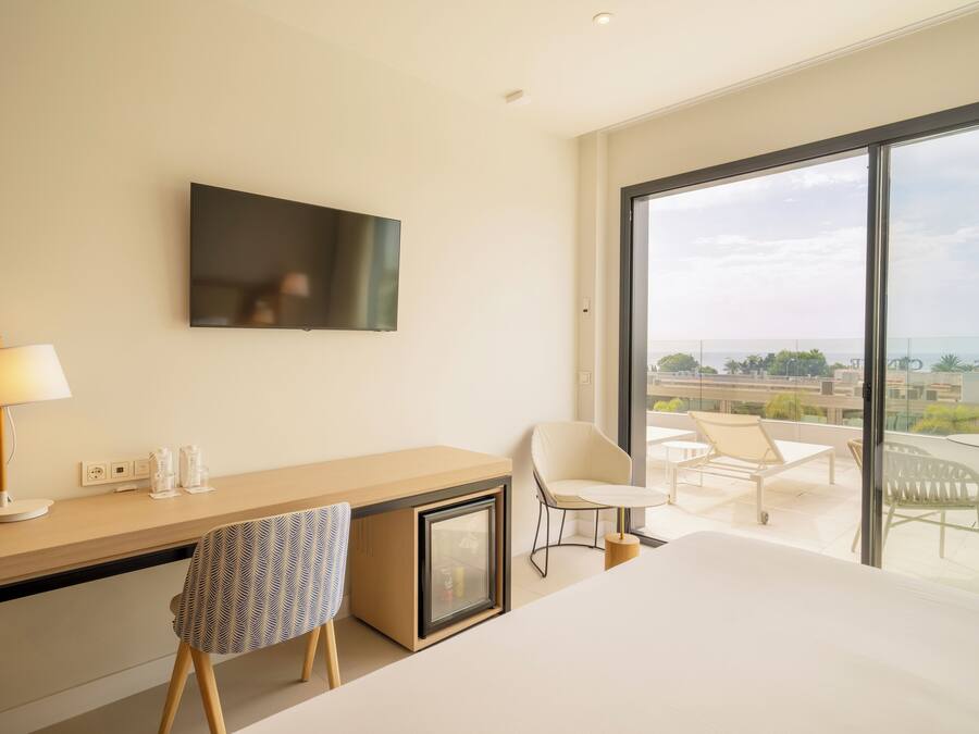 Habitación de hotel con escritorio, silla, cama y un amplio ventanal con vistas a la ciudad.