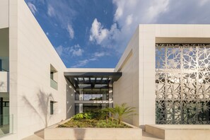 A modern building with a glass facade, a courtyard with plants, and a decorative screen.