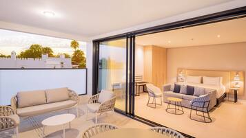 A modern hotel room with a balcony, a sofa, a dining table, and a bed.