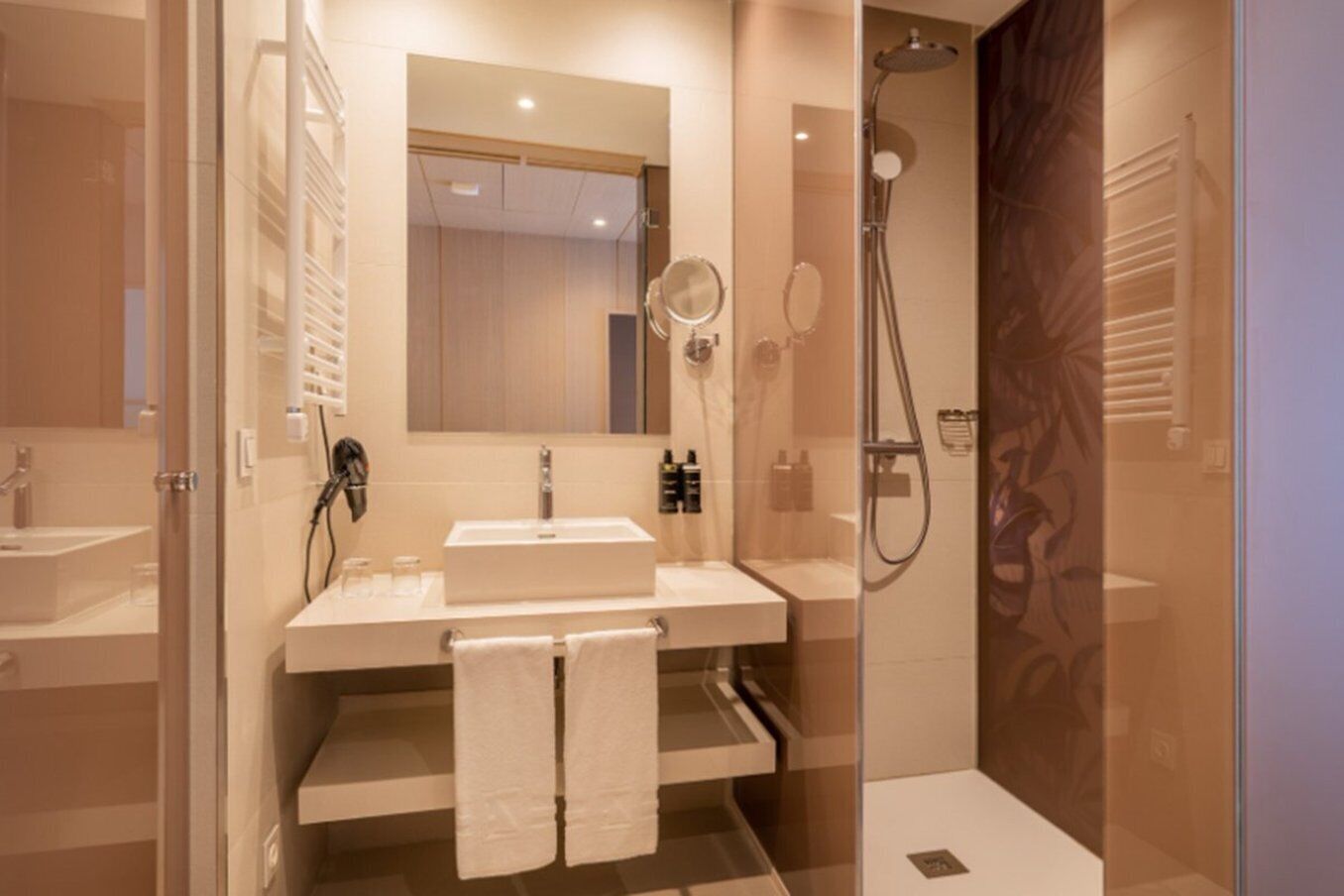 A modern bathroom with a double sink, a large mirror, a shower enclosure, and a towel rack.
