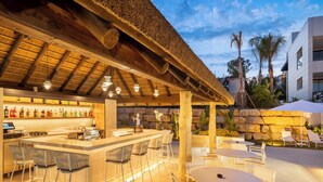 Un área de bar al aire libre con techo de paja, taburetes y mesas.