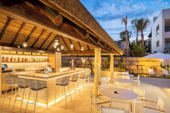 An outdoor bar area with a thatched roof, bar stools, and tables.