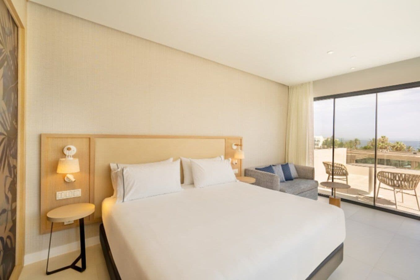 Habitación de hotel con una cama grande, un sofá, una mesita y un balcón con vistas.