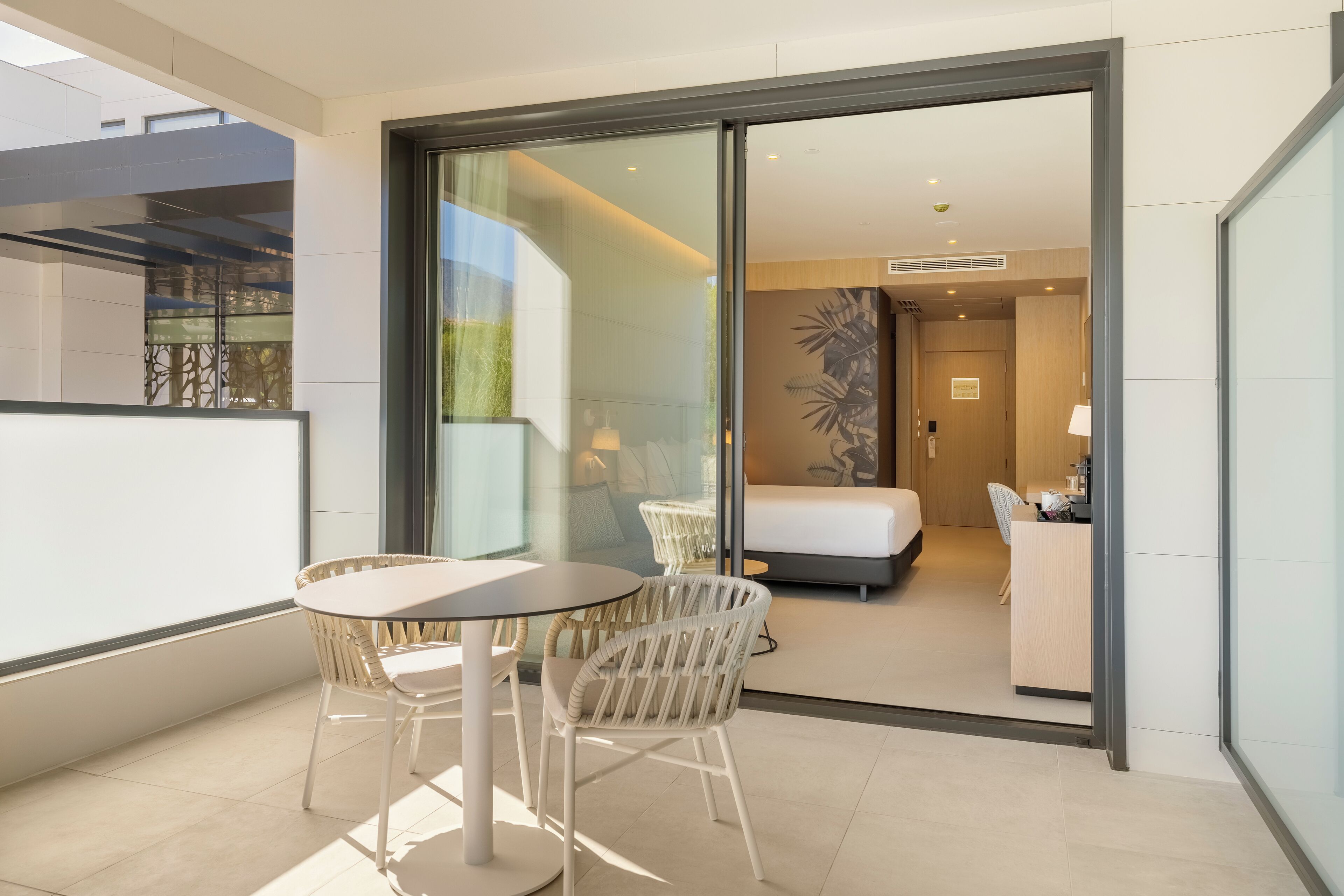 Une chambre d’hôtel moderne, équipée d’un lit, d’un bureau et d’une chaise. Elle dispose également d’un balcon avec une table et des chaises.