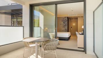 Een moderne hotelkamer met een bed, een bureau en een stoel. Er is een balkon met een tafel en stoelen.